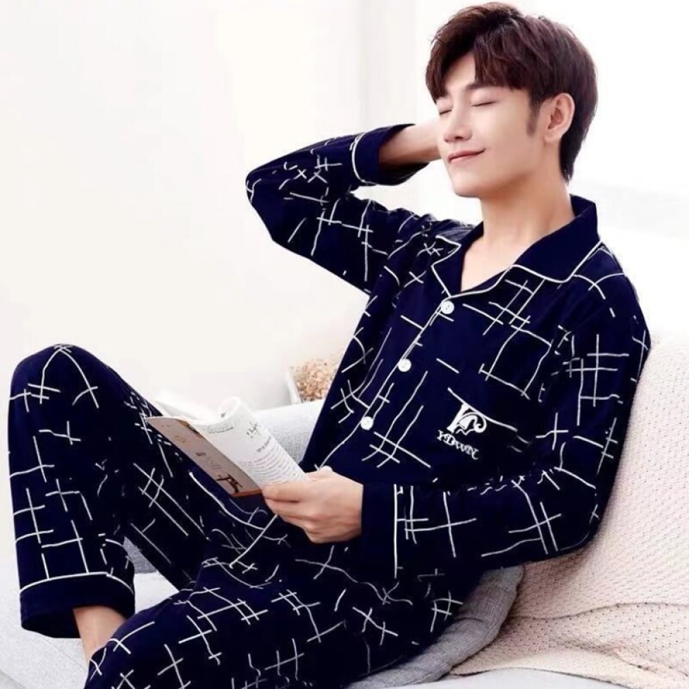 Lässiger nachtblauer Sommerpyjama aus Baumwolle für Männer, getragen von einem Mann, der auf einem Bett in einem Haus sitzt
