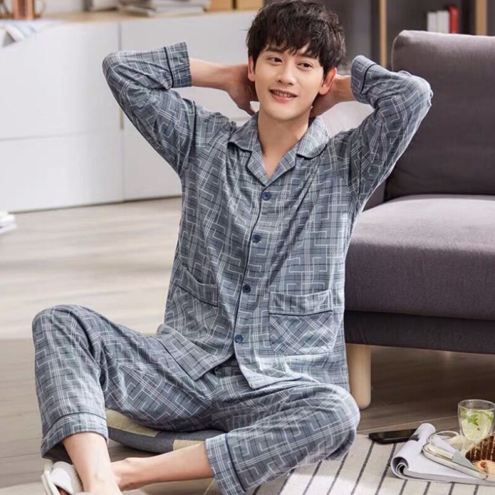 Grauer Umlegepyjama mit geometrischem Druck für Männer, der von einem Mann getragen wird, der auf einem Teppich in einem Haus sitzt