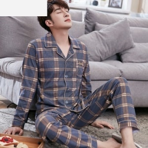 Modischer karierter Baumwollpyjama für Männer, getragen von einem Mann, der auf einem Teppich in einem Haus sitzt