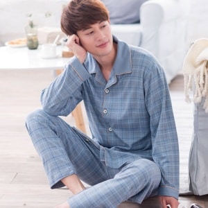 Himmelblau karierter Pyjama aus Baumwolle für Männer, der von einem Mann getragen wird, der auf einem Teppich in einem Haus sitzt