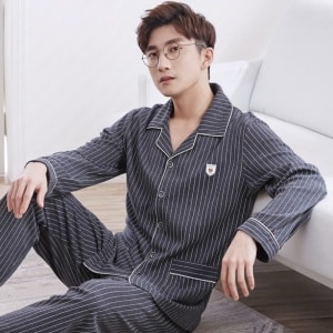 Beigefarbener, weißer gestreifter Sommerpyjama aus Baumwolle mit Umlegekragen für Männer, der von einem Mann getragen wird, der auf einem Teppich in einem Haus sitzt
