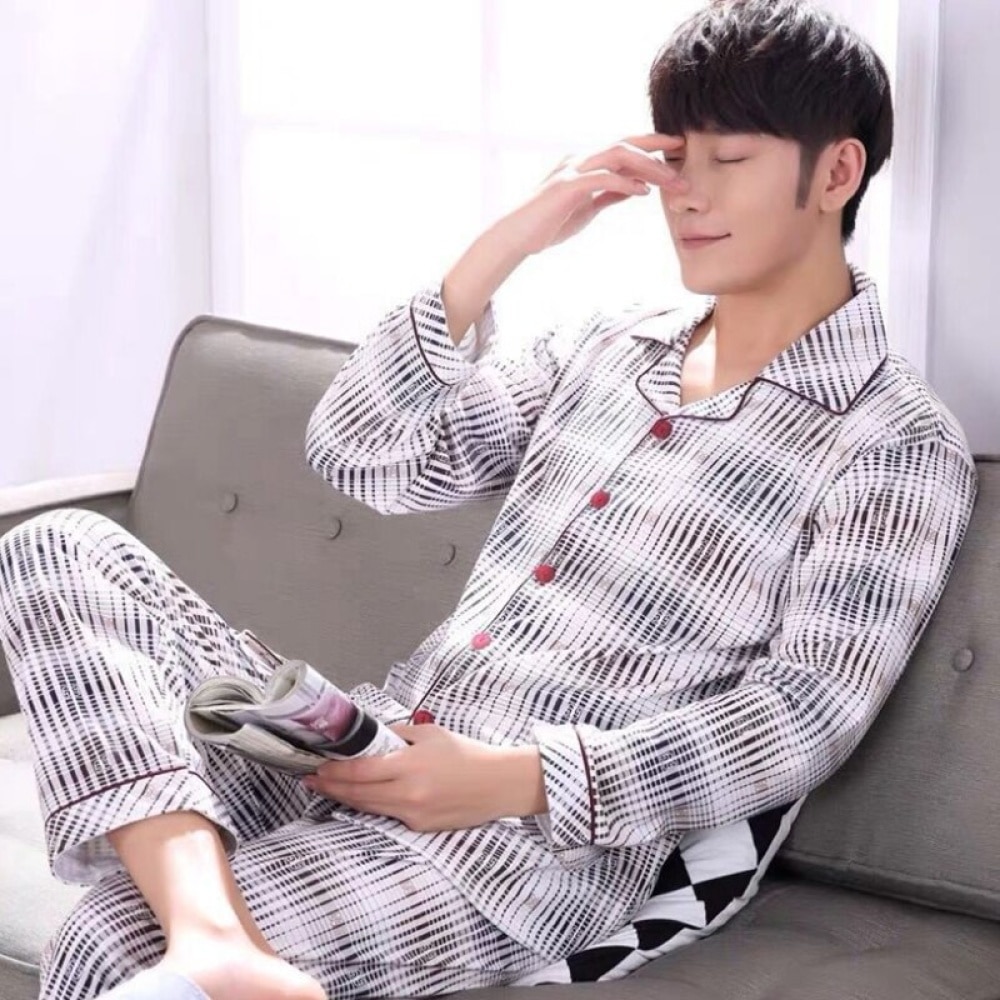 Weißer, schwarz gestreifter Umlegepyjama für Männer, der von einem Mann getragen wird, der auf einem Sofa in einem Haus sitzt