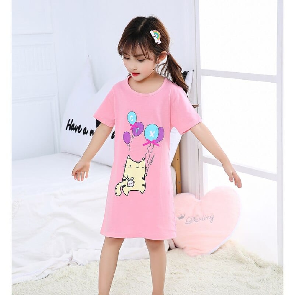 Pyjama-Nachtkleid aus Baumwolle mit Katzendruck, getragen von einem kleinen Mädchen auf einem Bett in einem Haus