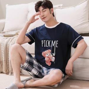 Sommerpyjama mit nachtblauem T-Shirt mit Bärenmuster und karierten Shorts, getragen von einem Mann, der auf einem Teppich in einem Haus sitzt