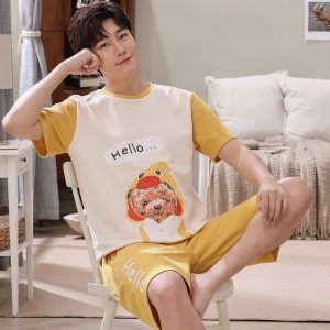 Sommerpyjama T-Shirt und Shorts aus Baumwolle mit Hundedruck, getragen von einem Mann, der auf einem Stuhl in einem Haus sitzt