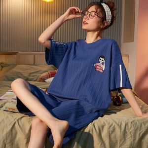 Pyjama-Nachtkleid aus dunkelblauer Baumwolle mit kurzen Ärmeln, getragen von einer Frau, die auf einem Bett in einem Haus sitzt