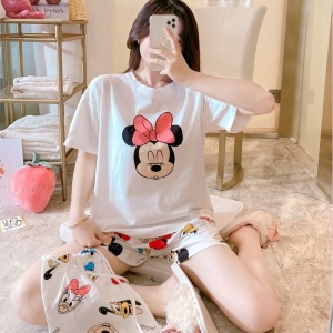 Sommer-Pyjama-Set aus Satin mit Minnie-Mouse-Print, getragen von einer Frau, die auf einem Bett in einem Haus sitzt