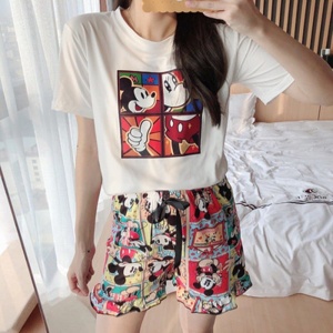 Sommerpyjama mit Mickey-Mouse-Print für Frauen, der von einer Frau vor einem Bett in einem Haus getragen wird