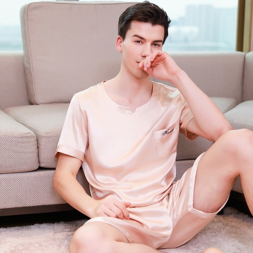 Champagnerfarbener zweiteiliger Pyjama aus Satin für Männer, der von einem Mann vor einem Sofa in einem Haus getragen wird
