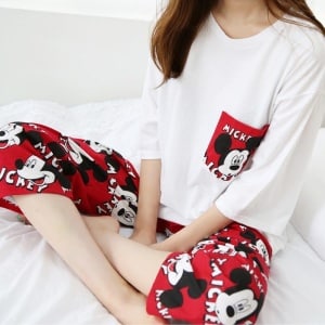 Zweiteiliger rot-weißer Pyjama mit Mickey-Mouse-Muster, getragen von einer Frau, die auf einem modischen Bett sitzt