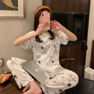 Zweiteiliger Pyjama mit kurzen Ärmeln und Hundemotiv, getragen von einer sitzenden Frau, die ein Foto in einem Haus macht