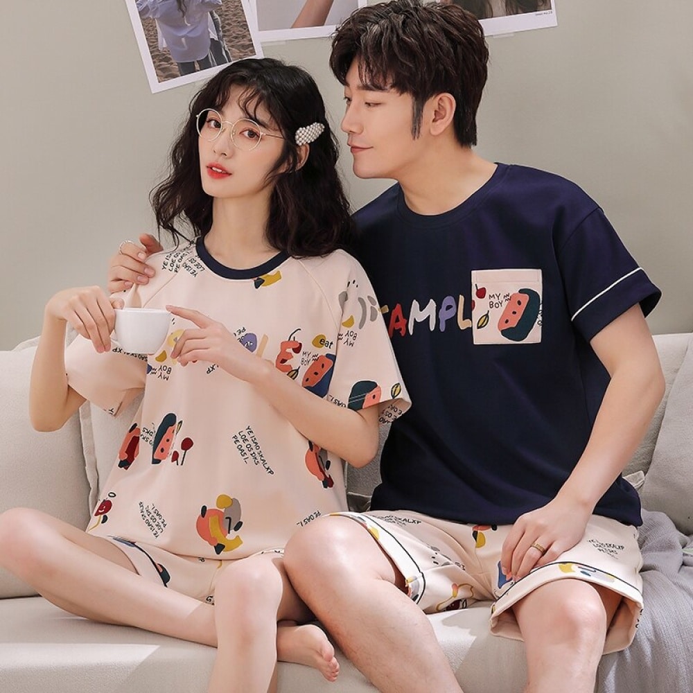 Zweiteiliger Baumwollpyjama mit T-Shirt und Shorts mit Comicmuster, getragen von einem Paar auf einem Sofa in einem Haus