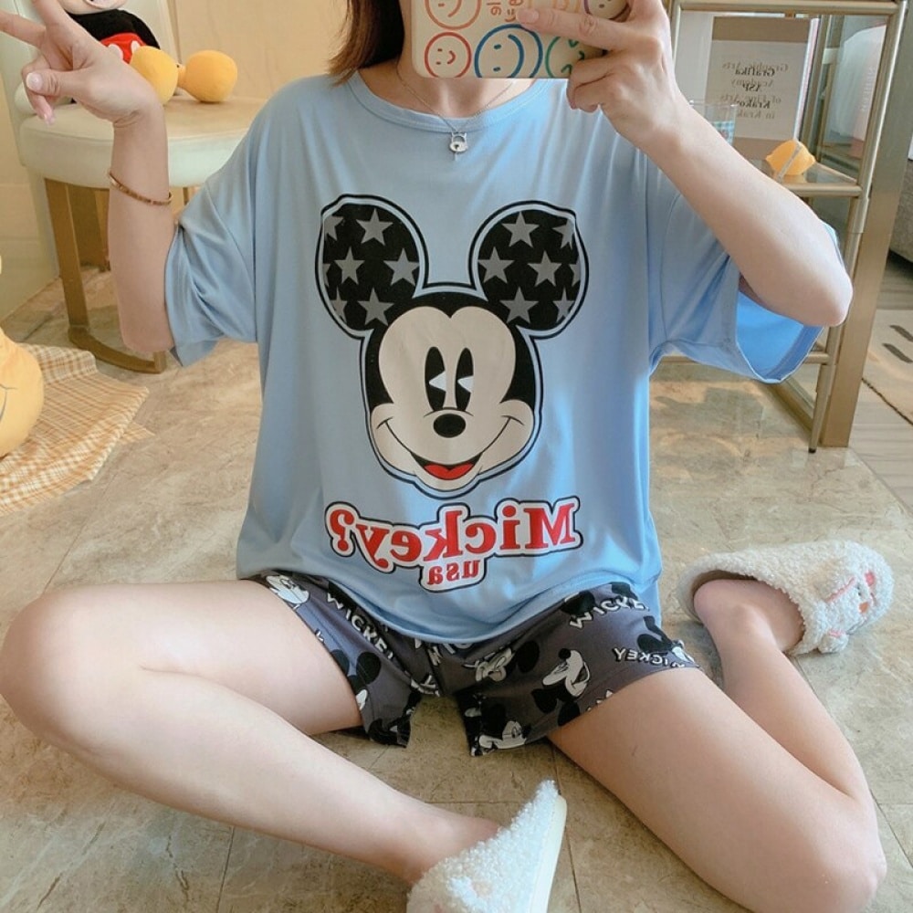 Pyjama aus blauem T-Shirt mit Mickey-Mouse-Muster und modischen grauen Shorts, getragen von einer Frau, die auf einem Teppich in einem Haus sitzt
