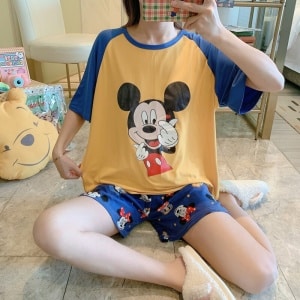 Zweiteiliger Pyjama mit T-Shirt und Shorts mit Mickey-Mouse-Muster, getragen von einer Frau, die auf einem Foto in einem Haus sitzt