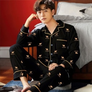 Kamelpyjama aus Baumwolle, getragen von einem Mann, der auf einem Teppich vor einem Bett in einem Haus sitzt
