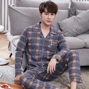 Doppelkarierter Pyjama für Männer, getragen von einem Mann, der auf einem Teppich vor einem Sofa in einem Haus sitzt