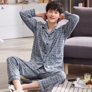 Grau gestreifter Baumwollpyjama für Männer, getragen von einem Mann, der auf einem Teppich vor einem Sofa in einem Haus sitzt