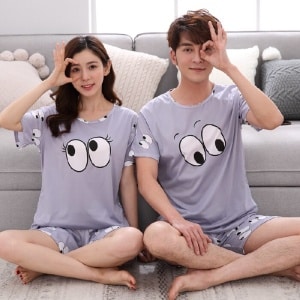 Pyjama-Set mit Augenmotiv für ein Paar, getragen von einem Paar, das auf einem Teppich in einem Haus sitzt