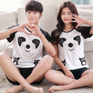 Pyjama für Paare mit Pandamuster, getragen von einem Paar, das auf einem Teppich vor einem Sofa in einem Haus sitzt