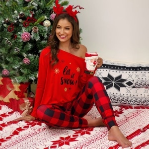 Bedruckter Weihnachtspyjama für Frauen mit freien Schultern, getragen von einer Frau, die auf einem Teppich vor einem Weihnachtsbaum in einem Haus sitzt