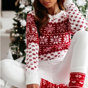 Weihnachtspullover mit Schneeflockenmuster für eine Frau, die von einer Frau getragen wird, die vor einem Weihnachtsbaum in einem Haus sitzt
