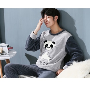 Herrenpyjama mit Panda-Muster, getragen von einem Mann, der auf einem Sofa in einem Haus sitzt