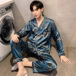 Bläulicher satinierter Herrenpyjama, der von einem Mann getragen wird, der in einem Haus vor einer Waschmaschine sitzt