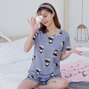 Sommerpyjama mit T-Shirt und grauen Shorts für Frauen mit Kaninchenaufdruck, getragen von einer Frau, die auf einem Bett in einem Haus sitzt