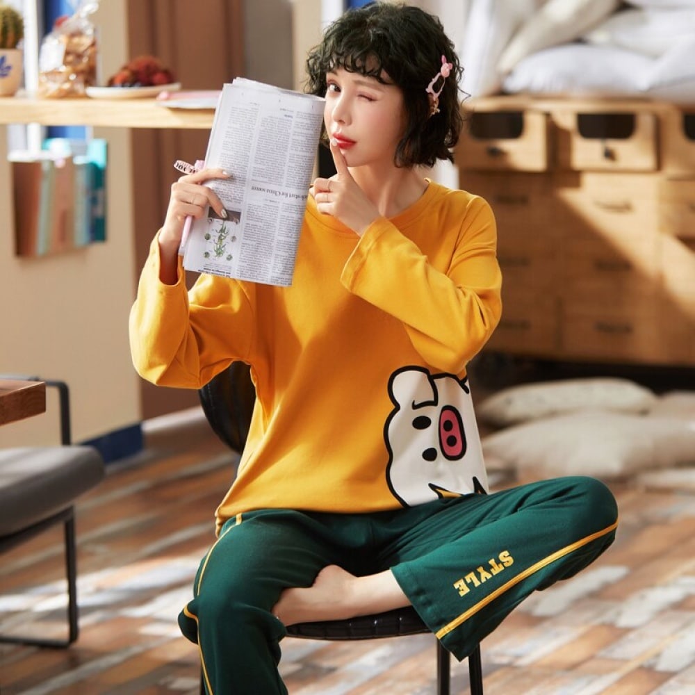 Baumwollpyjama mit gelbem Pullover mit Schweinchenmuster und grüner Hose, getragen von einer Frau auf einem Stuhl, die in einem Haus eine Gazette las