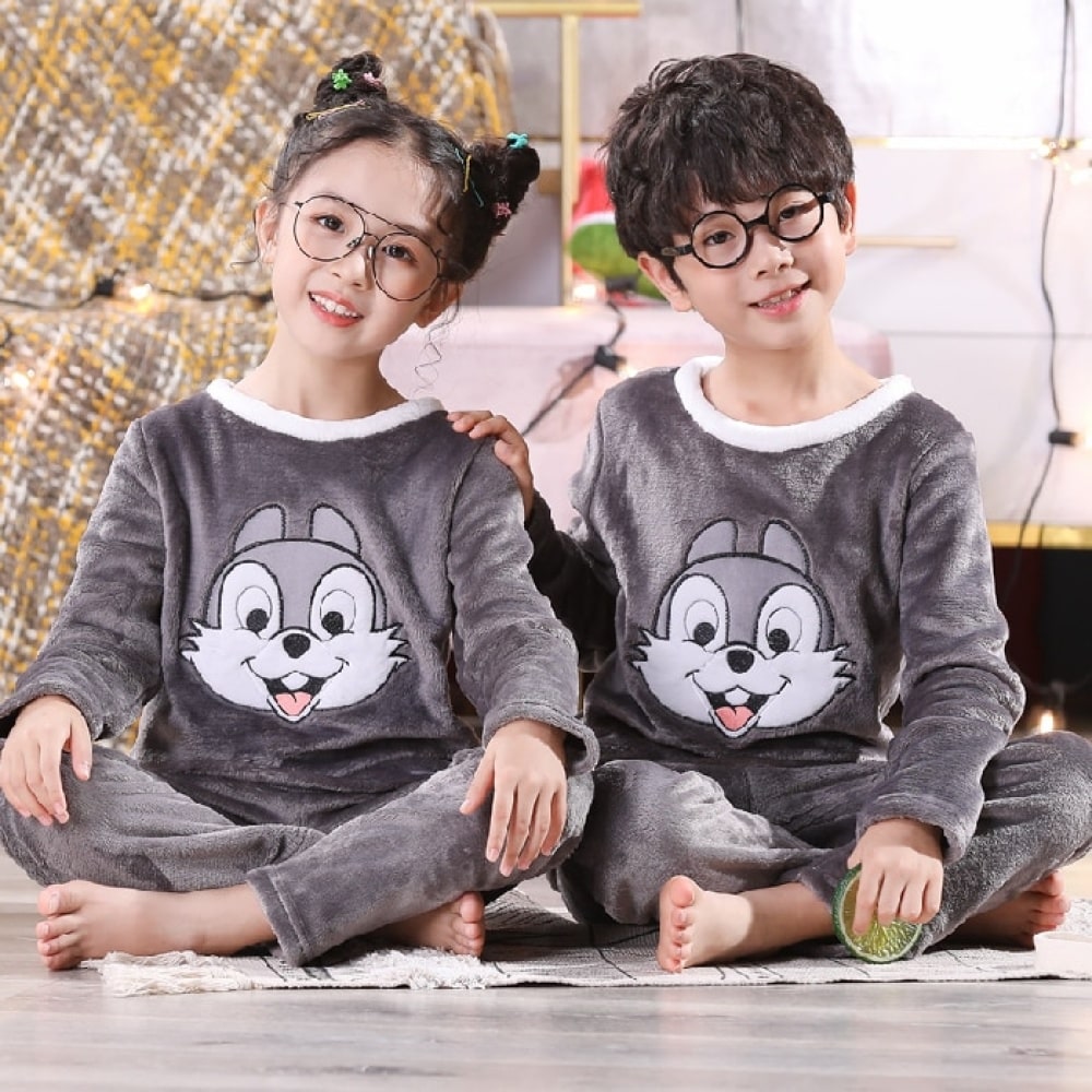 Panpan-Kinderpyjama aus Flanell mit Kaninchenmotiv, getragen von einem kleinen Jungen und einem kleinen Mädchen, die auf einem Teppich vor einem Nachttisch in einem Haus sitzen