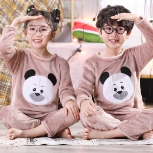 Langärmeliger Kinderpyjama aus Flanell mit Panda-Print, getragen von einem kleinen Jungen und einem kleinen Mädchen, die auf einem Teppich in einem Haus sitzen