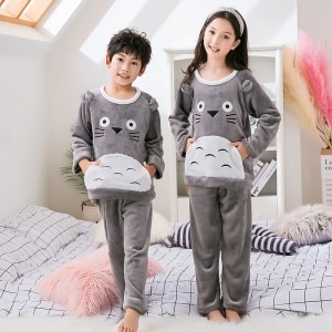 Grauer Kinderpyjama aus Flanellfleece mit Toroto-Druck, getragen von einem kleinen Jungen und einem kleinen Mädchen, das einen Kopfbügel auf einem Bett in einem Haus trägt