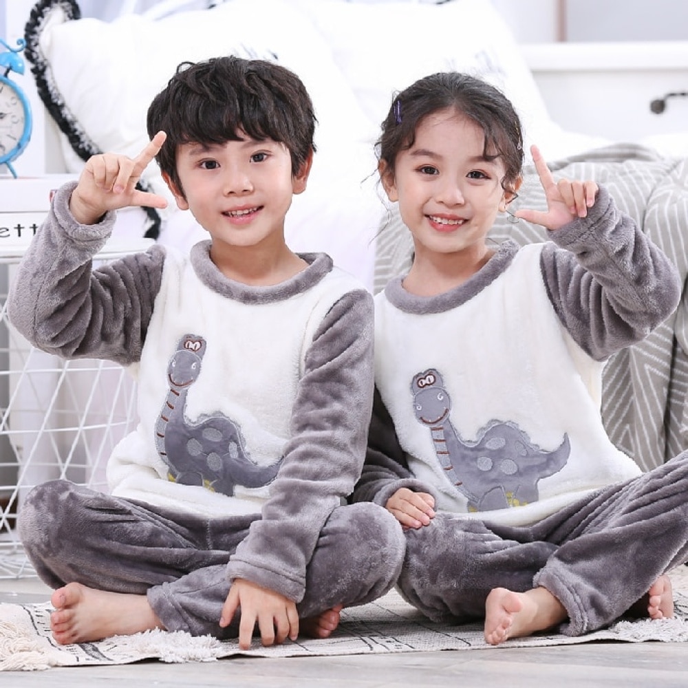 Zweiteiliger grauer Kinderpyjama aus Flanell mit Dinosauriermotiv, der von einem Jungen und einem Mädchen in einem Haus getragen wird