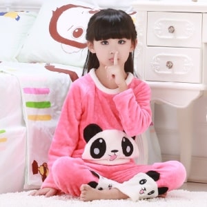 Zweiteiliger rosa Pyjama mit Panda-Muster für Mädchen, getragen von einem kleinen Mädchen, das auf einem Teppich vor einem Bett in einem Haus sitzt