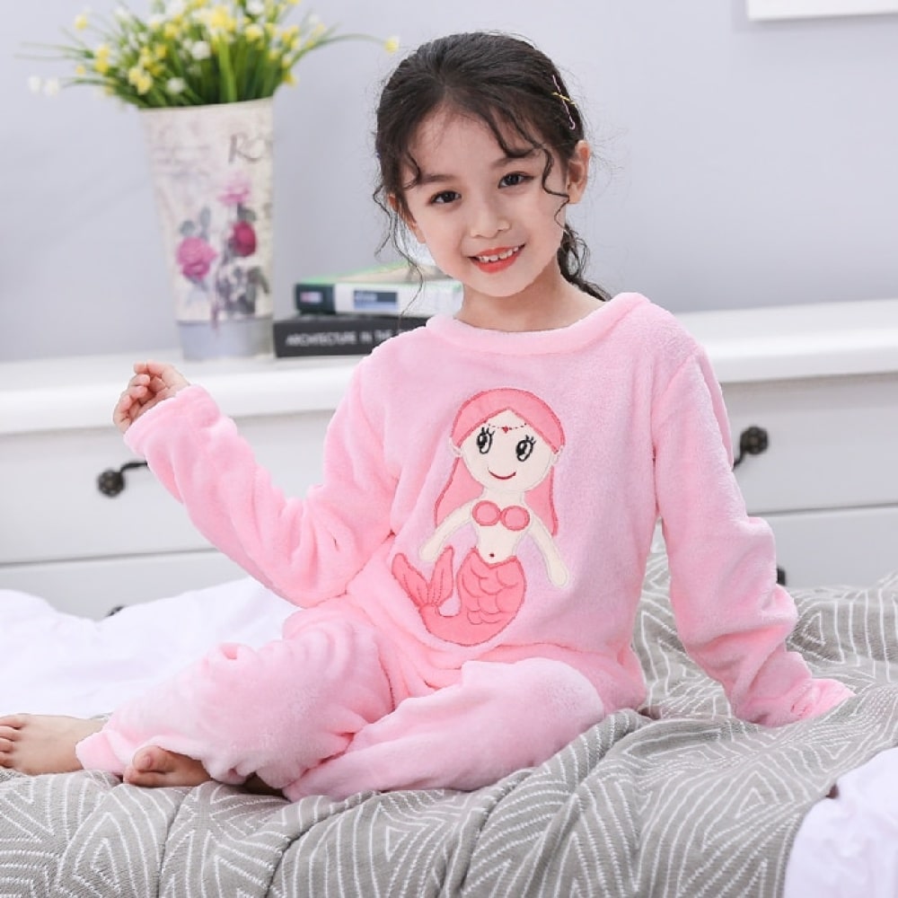 Langärmeliger Flanellpyjama mit Meerjungfrauenmuster für ein Mädchen, das von einem kleinen Mädchen auf ein Bett in einem Haus getragen wird