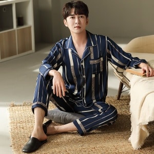 Blauer, goldgestreifter, langärmeliger Baumwollpyjama, getragen von einem Mann, der auf einem Teppich in einem Haus sitzt