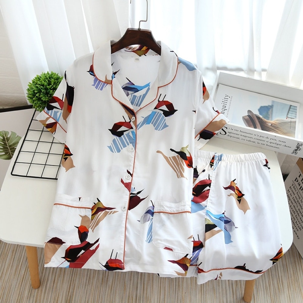 Weißer Sommerpyjama mit kurzen Ärmeln und Vogeldruck für Frauen auf einem Tisch mit einer Zeitschrift als Dekoration