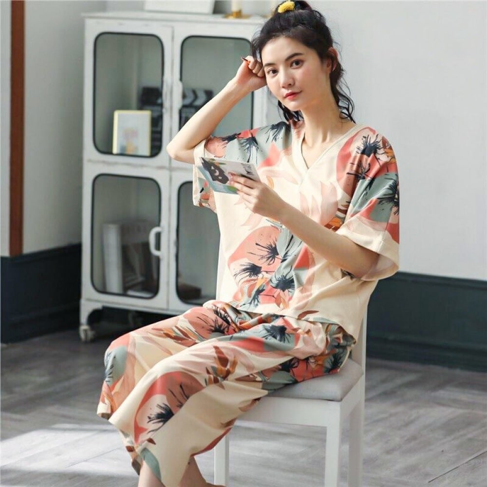 Zweiteiliger Sommerpyjama mit V-Ausschnitt und Blumenmuster, getragen von einer Frau, die auf einem Stuhl in einem Haus sitzt
