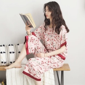 Damenpyjama mit Fledermausärmeln und rotem Blumendruck, getragen von einer Frau, die ein Buch liest und auf einem Stuhl in einem Haus sitzt