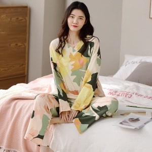 Langärmeliger Damenpyjama mit V-Ausschnitt und Blumenmuster, getragen von einer Frau, die auf einem Bett in einem Haus sitzt