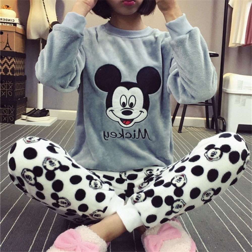 Zweiteiliger Pyjama mit Mickey, das Oberteil ist ein grauer Pullover mit Mickey's Kopf und das Unterteil ist eine Hose mit schwarzen Mickey's Kopf, er wird von einer jungen Frau getragen