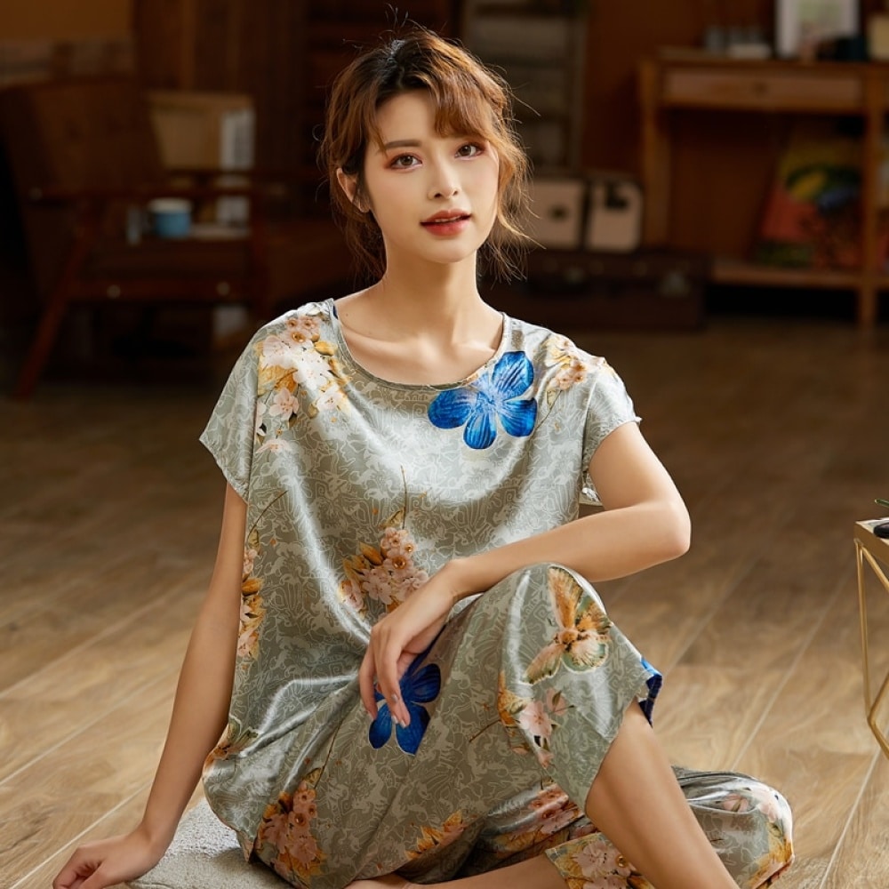Zweiteiliger grauer Sommerpyjama aus Seidensatin mit modischem Blumenmuster, getragen von einer Frau, die auf einem Teppich in einem Haus sitzt