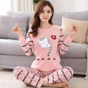 Niedlicher zweiteiliger Pyjama mit langen Ärmeln für Frauen, der von einer Frau getragen wird, die auf einem Teppich vor einem Stuhl in einem Haus sitzt