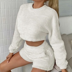 Pyjashort für Frauen mit weißem Sweatshirt, getragen von einer Frau, die auf einem Bett in einem Haus sitzt