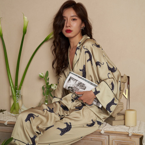 Beigefarbener Pyjama mit Leopardenmuster, getragen von einer Frau, die auf einem Möbelstück sitzt und eine Zeitschrift vor einer beigen Wand hält