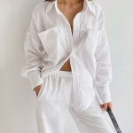Weißer Baumwollpyjama, der von einer Frau an einer weißen Wand getragen wird