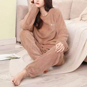 die junge Frau trägt einen beigefarbenen Pilou-Pilou-Pyjama und sitzt auf einer Decke neben einem Sofa auf dem Boden, ihr Kinn in einer ihrer Hände gestützt
