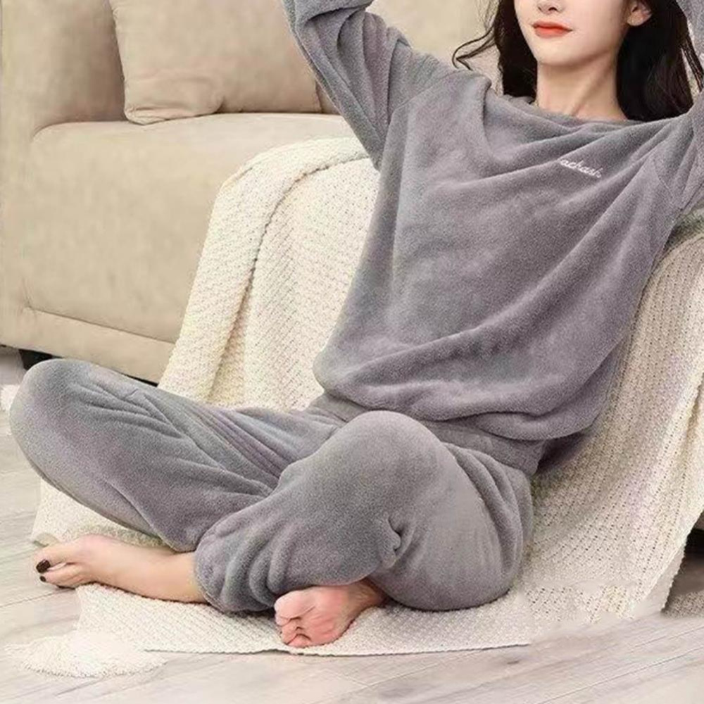 die junge Frau trägt einen grauen Pilou-Pilou-Pyjama und sitzt auf einer Decke neben einem Sofa auf dem Boden, die Hände hinter dem Kopf verschränkt