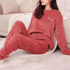 junge Frau trägt einen roten Pilou-Pilou-Pyjama, sie sitzt auf einer Decke neben einem Sofa auf dem Boden